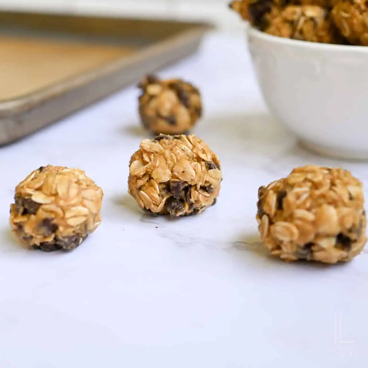 three peanut butter balls on a counter, with a bowl and baking sheet in the background.