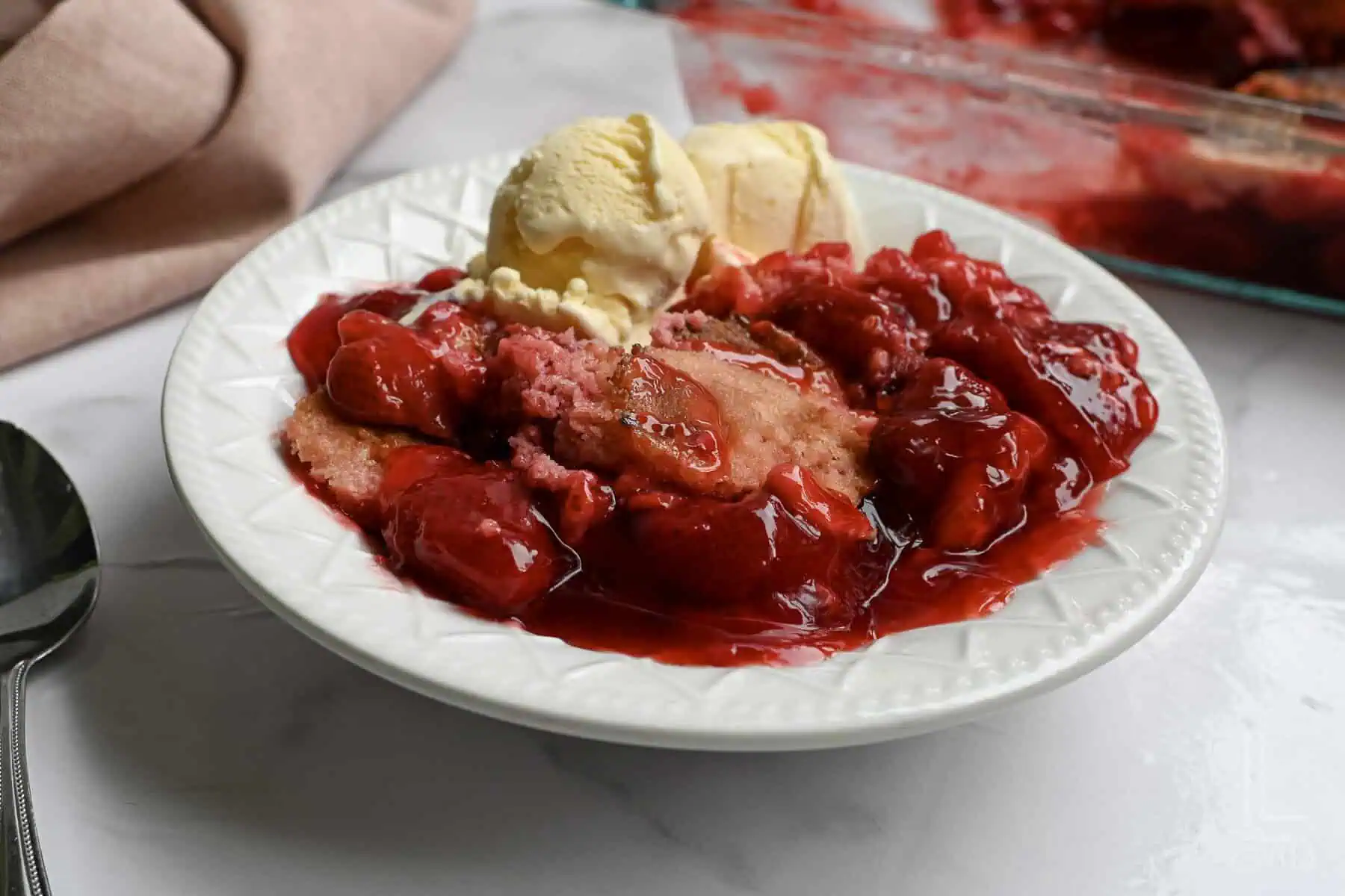 strawberry dump cake in a bowl with ice cream.