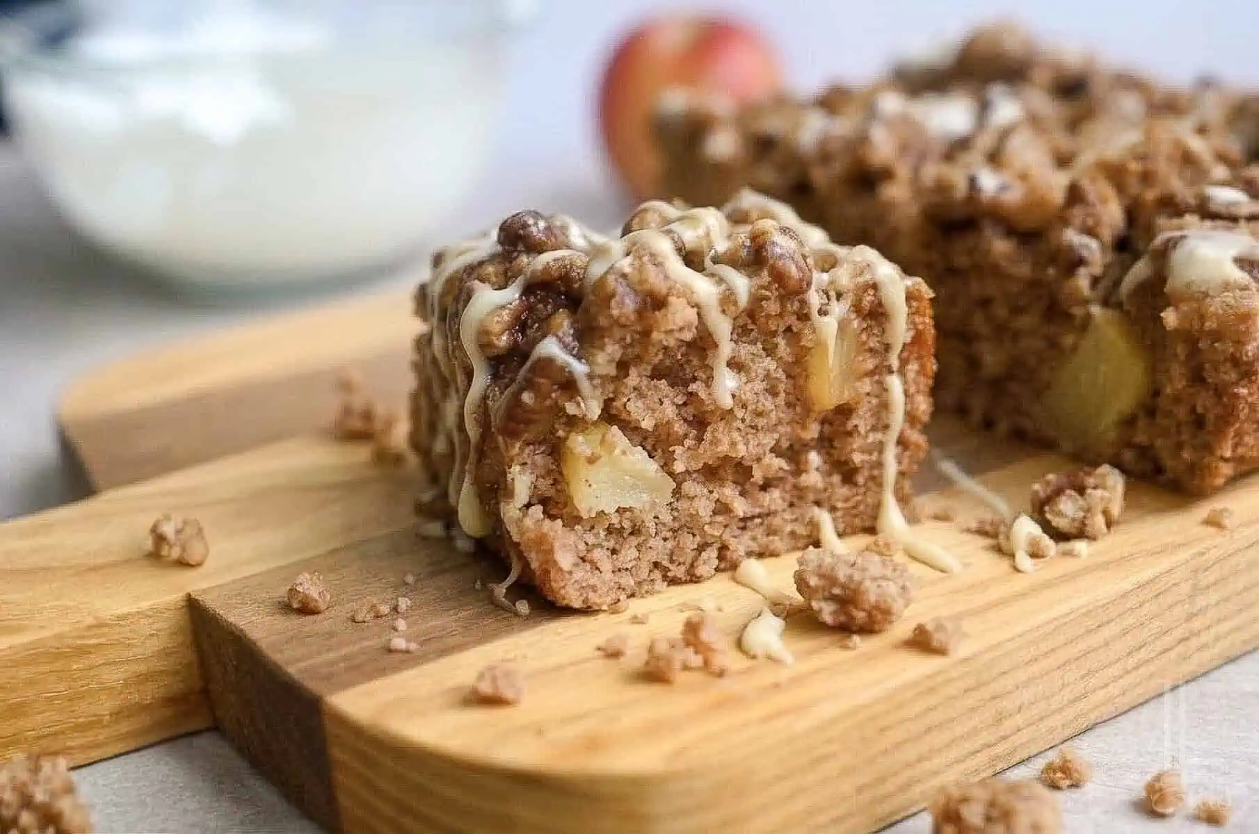 a piece of apple spice cake on a cutting board, surrounded by crumbs, drizzled with glaze and caramel sauce.