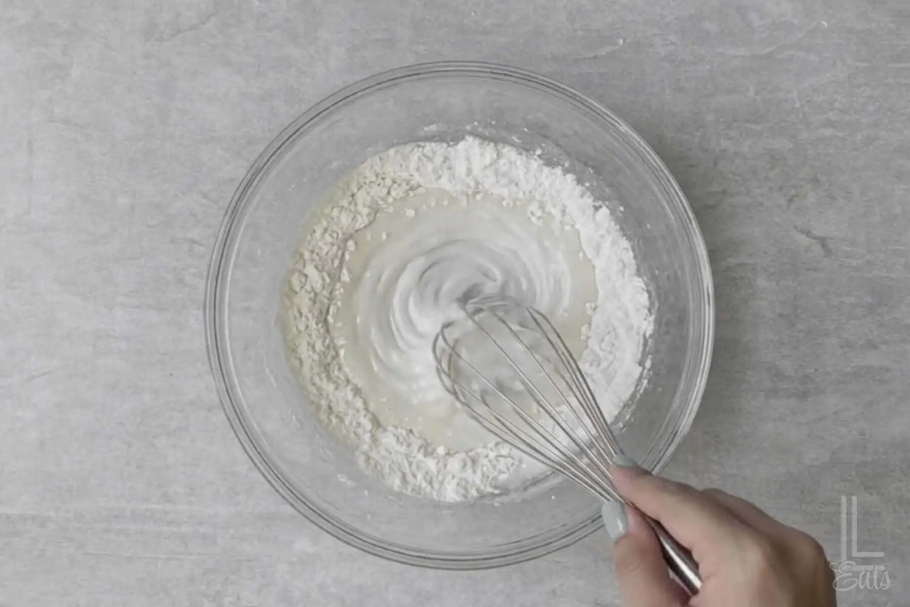 whisking powdered sugar and milk together in a glass bowl.