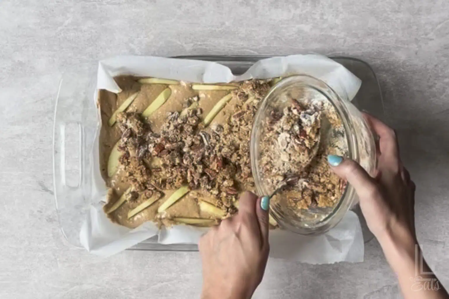 pouring the pecan crumble mixture over the top of the apple spice cake batter.
