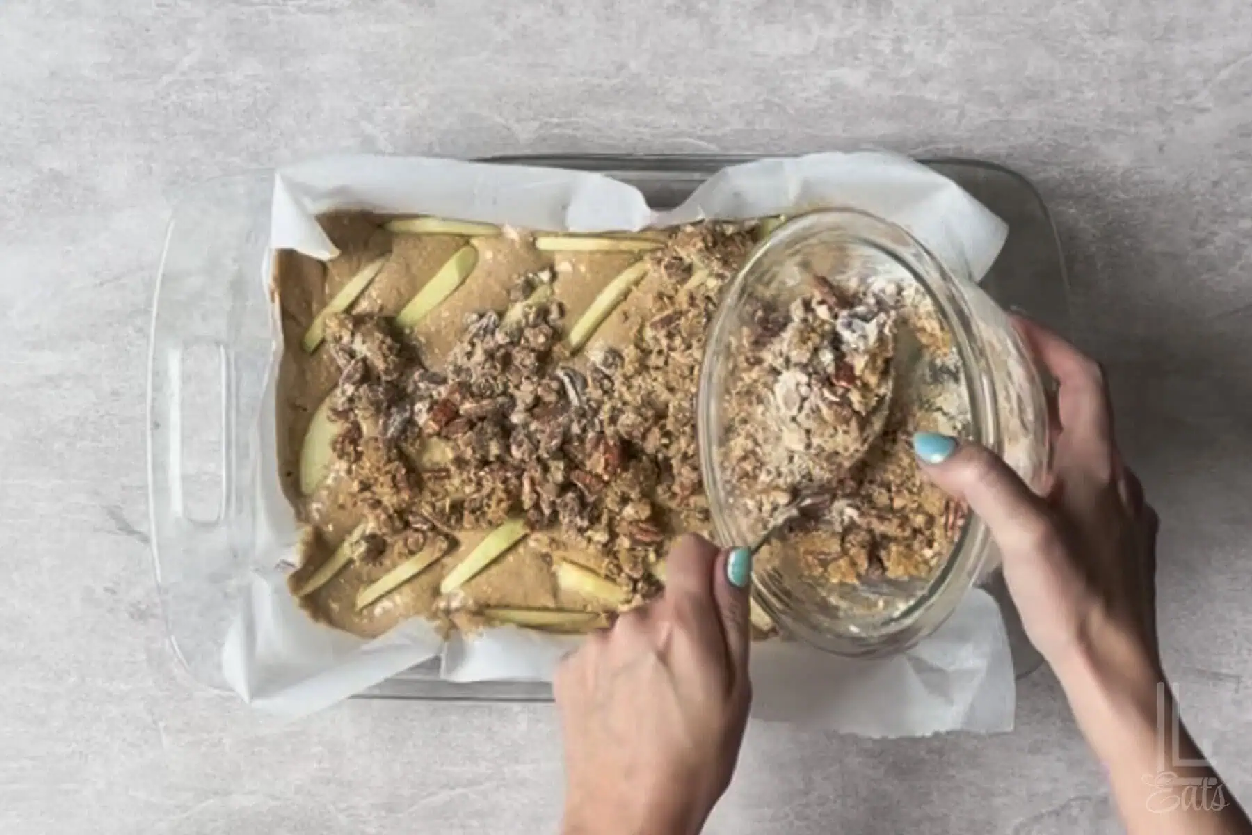 pouring the pecan crumble mixture over the top of the apple spice cake batter.