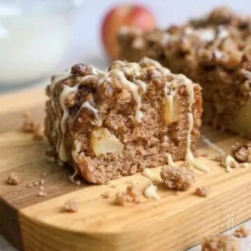 a piece of apple spice cake on a cutting board, surrounded by crumbs, drizzled with glaze and caramel sauce.
