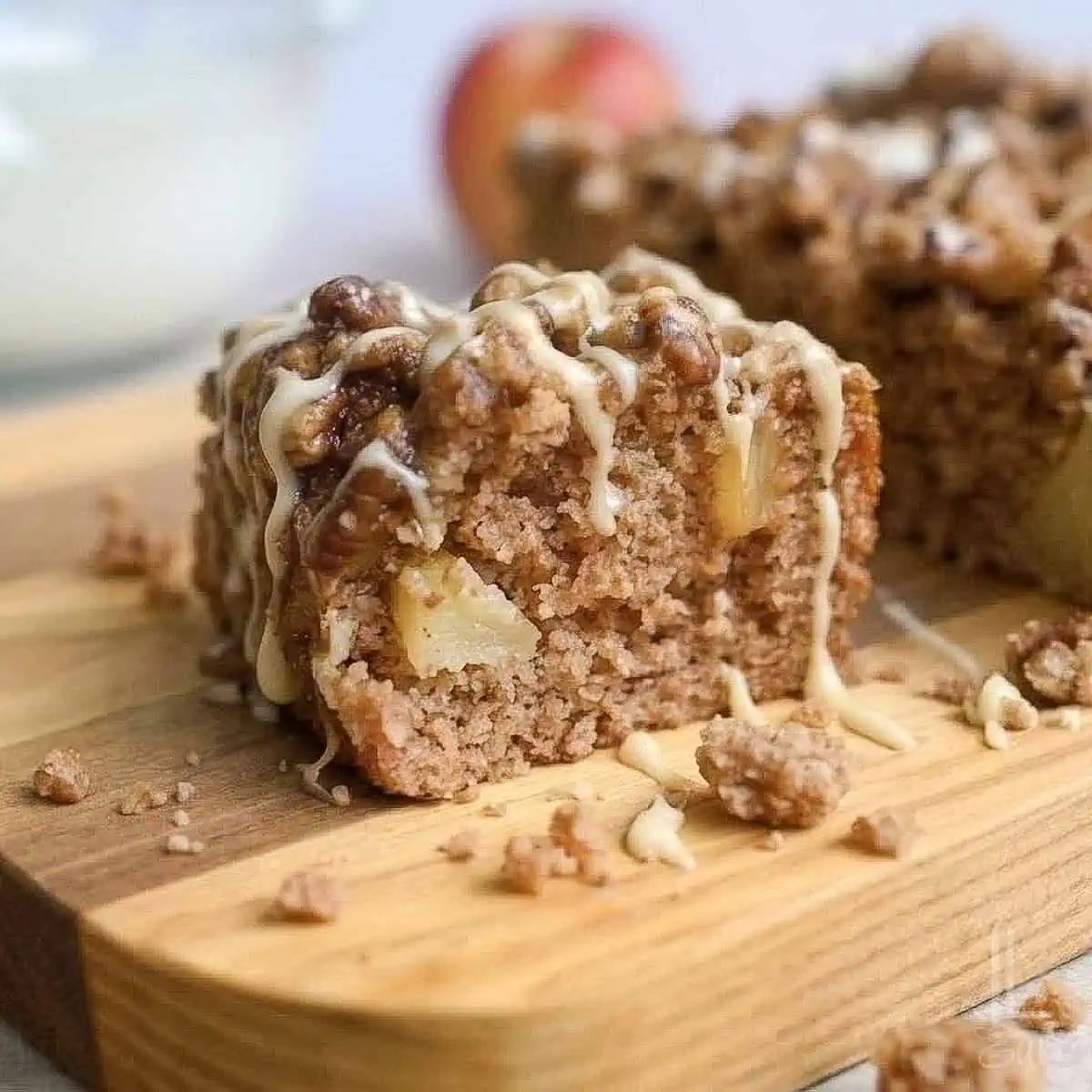 a piece of apple spice cake on a cutting board, surrounded by crumbs, drizzled with glaze and caramel sauce.