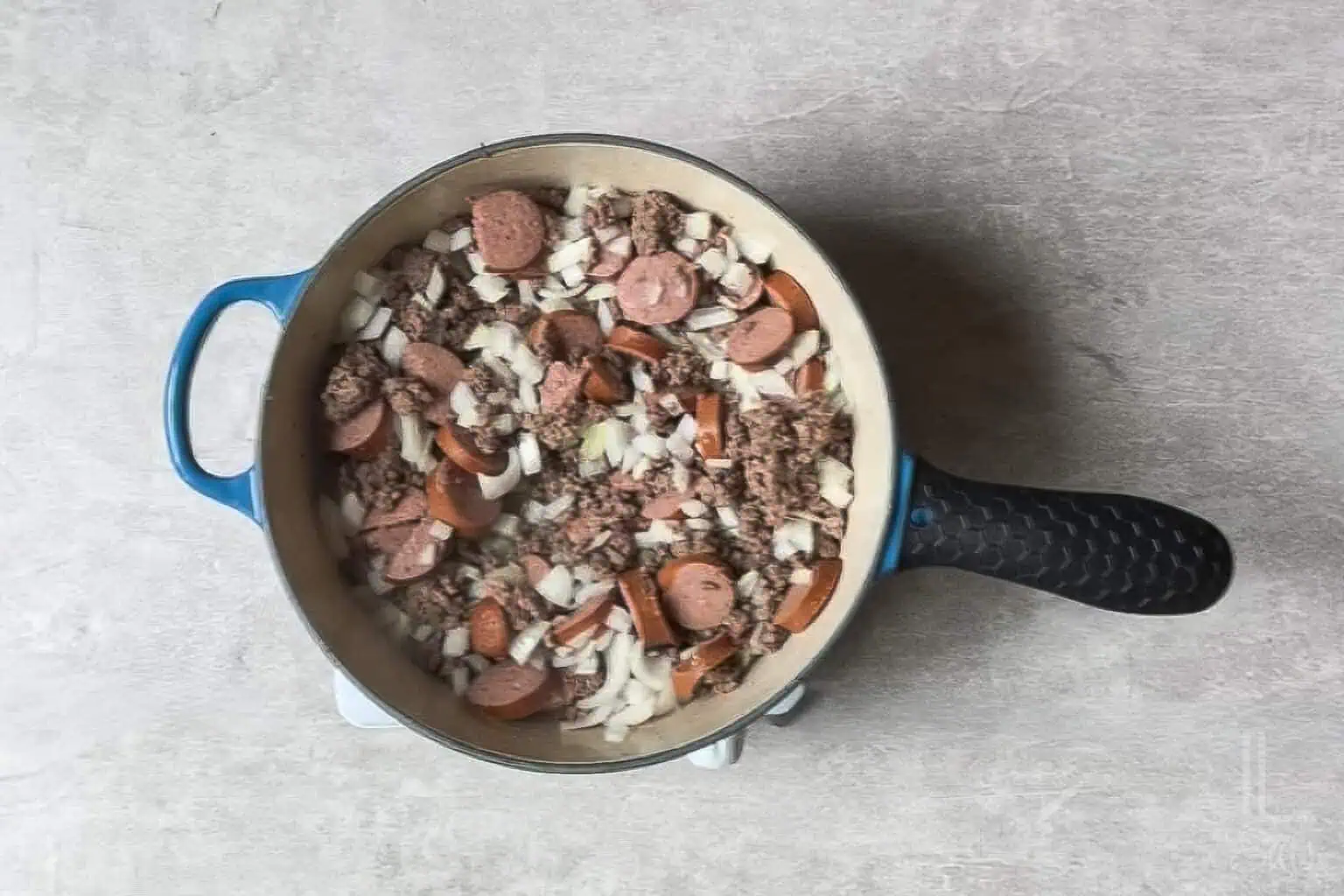 cooking kielbasa sausage, ground beef, and onion in a large pot.