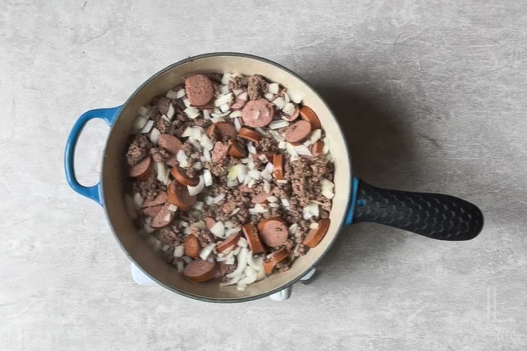 cooking kielbasa sausage, ground beef, and onion in a large pot.