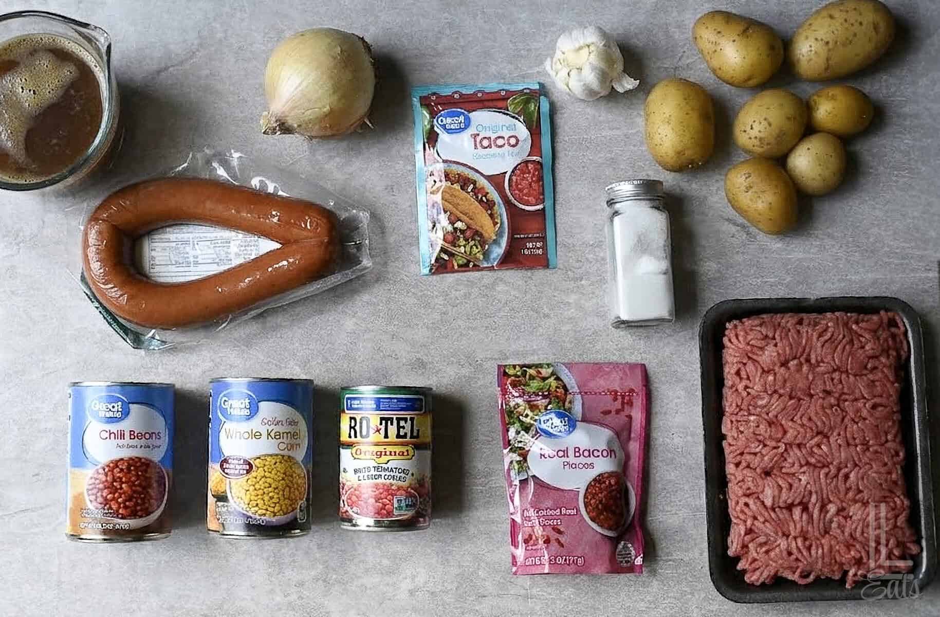 ingredients for cowboy stew, including ground beef, kielbasa sausage, potatoes, canned veggies, and taco seasoning.