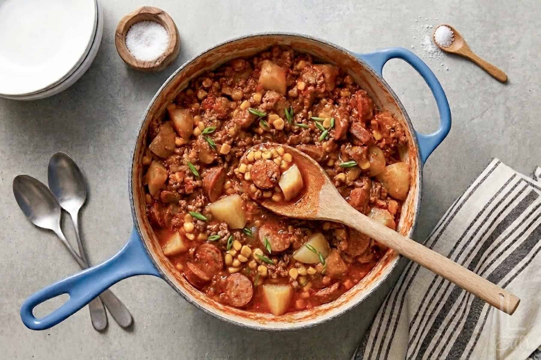a large pot of cowboy stew, showing potatoes, kielbasa sausage, ground beef, and corn in a hearty soup.