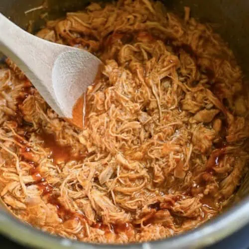 looking into a pot of instant pot pulled buffalo chicken, with a wooden spoon in it.