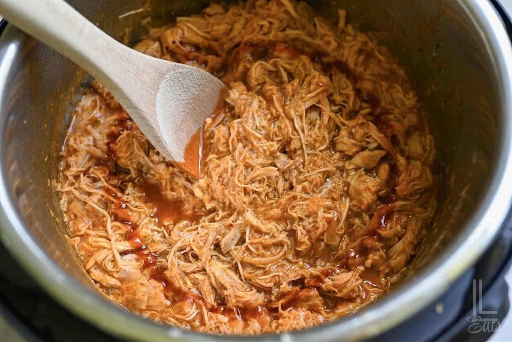 looking into a pot of instant pot pulled buffalo chicken, with a wooden spoon in it.