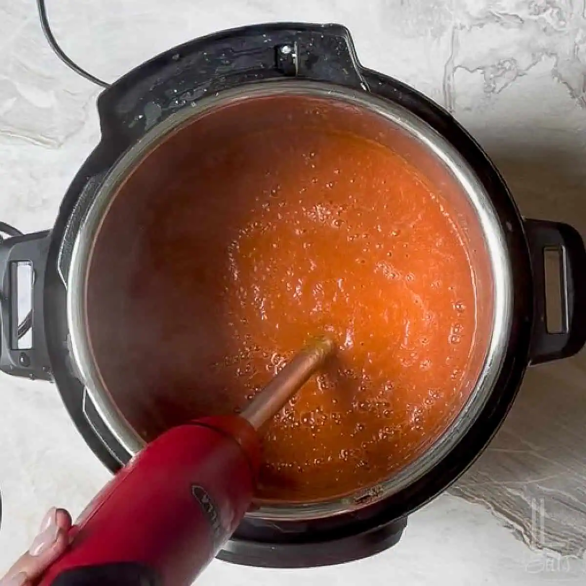 pureeing the instant pot tomato soup with a hand-held immersion blender.