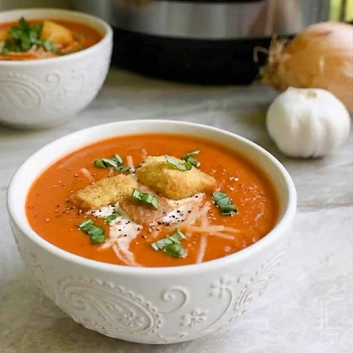 bowls of garnished tomato soup in front of an instant pot.
