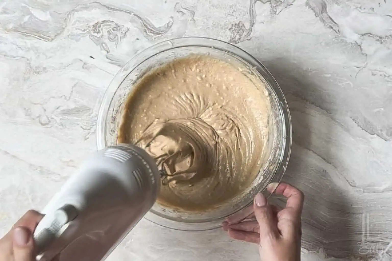 mixing the spice cake batter in a glass bowl with a hand mixer.