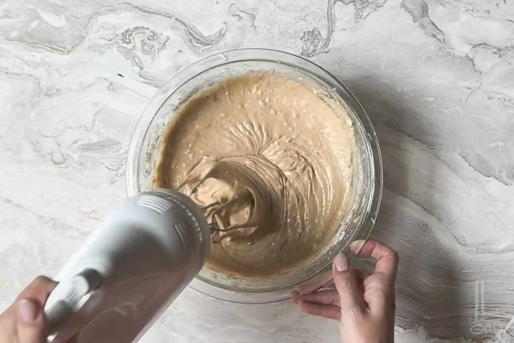 mixing the spice cake batter in a glass bowl with a hand mixer.