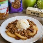 Apple crumble with pecans, oats, and vanilla ice cream on a white plate.