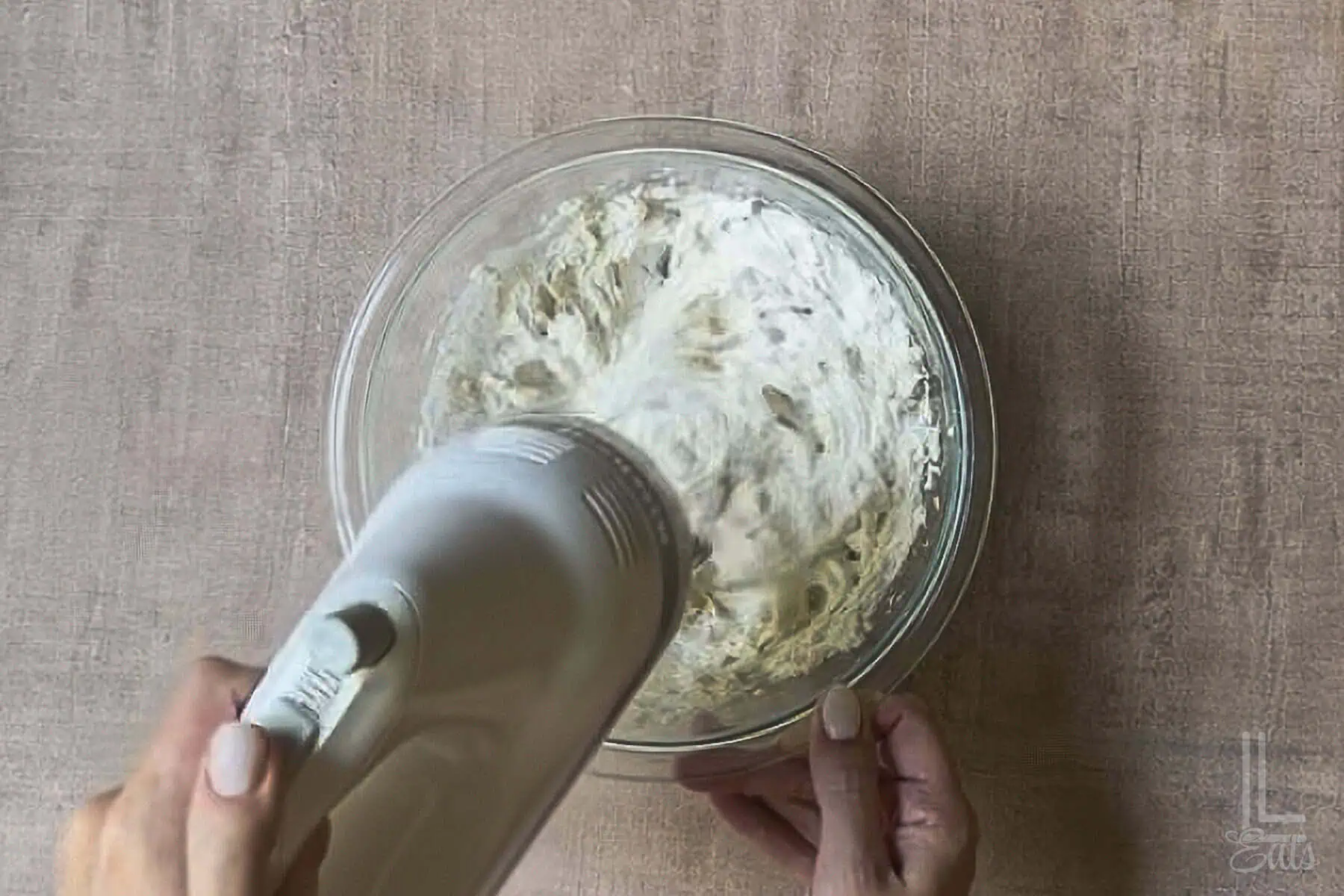 Mixing cream cheese and sour cream for creamy hot honey dip in a glass bowl with a hand blender.