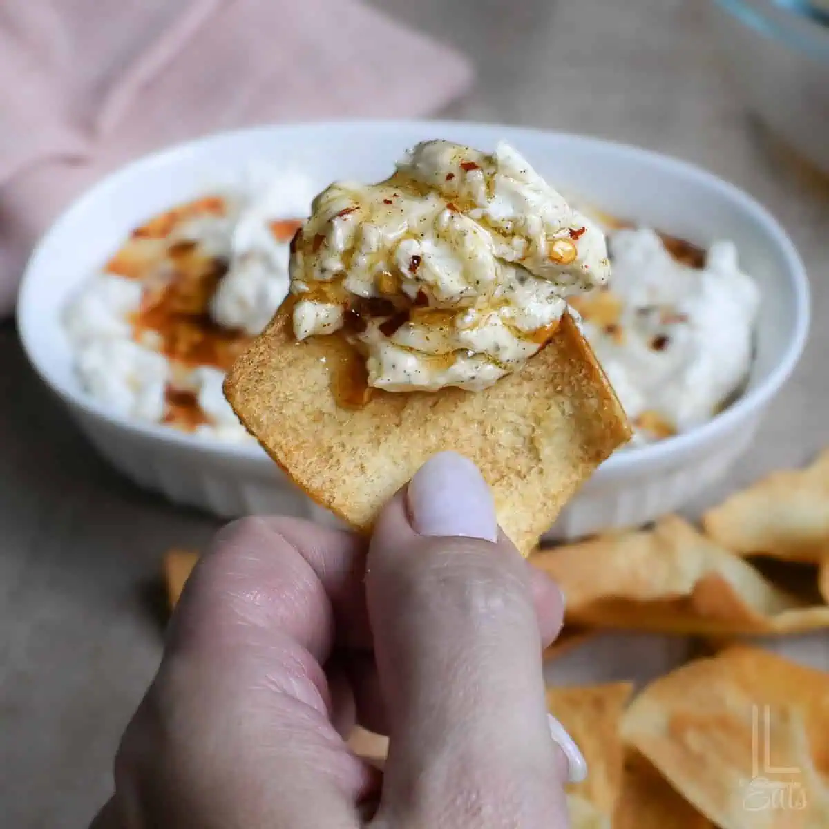 Creamy hot honey dip on a cracker with a baking dish in the background.