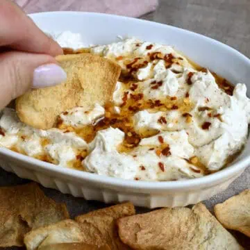 scooping out a bite of creamy hot honey dip with a pita chip.