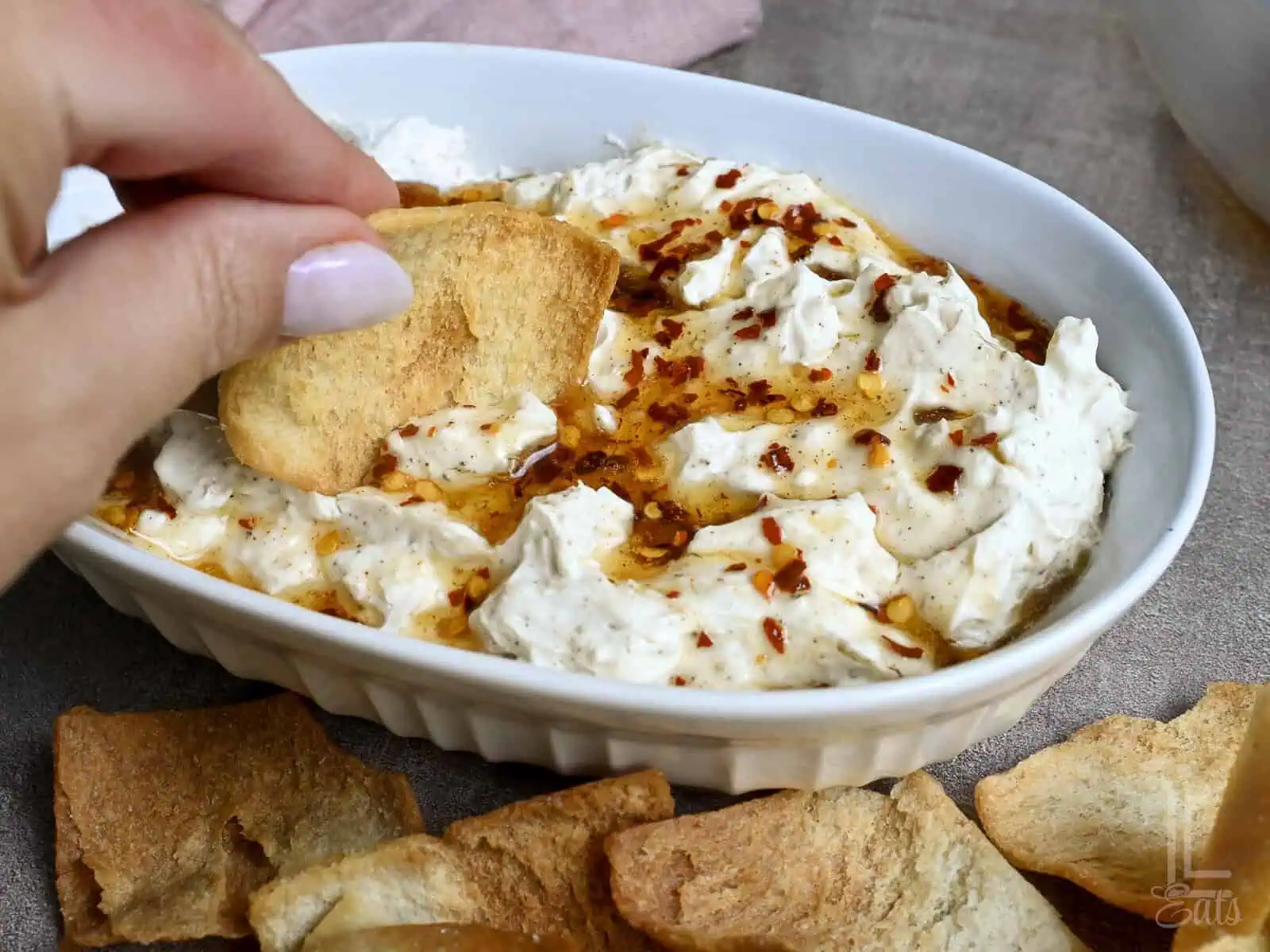 scooping out a bite of creamy hot honey dip with a pita chip.