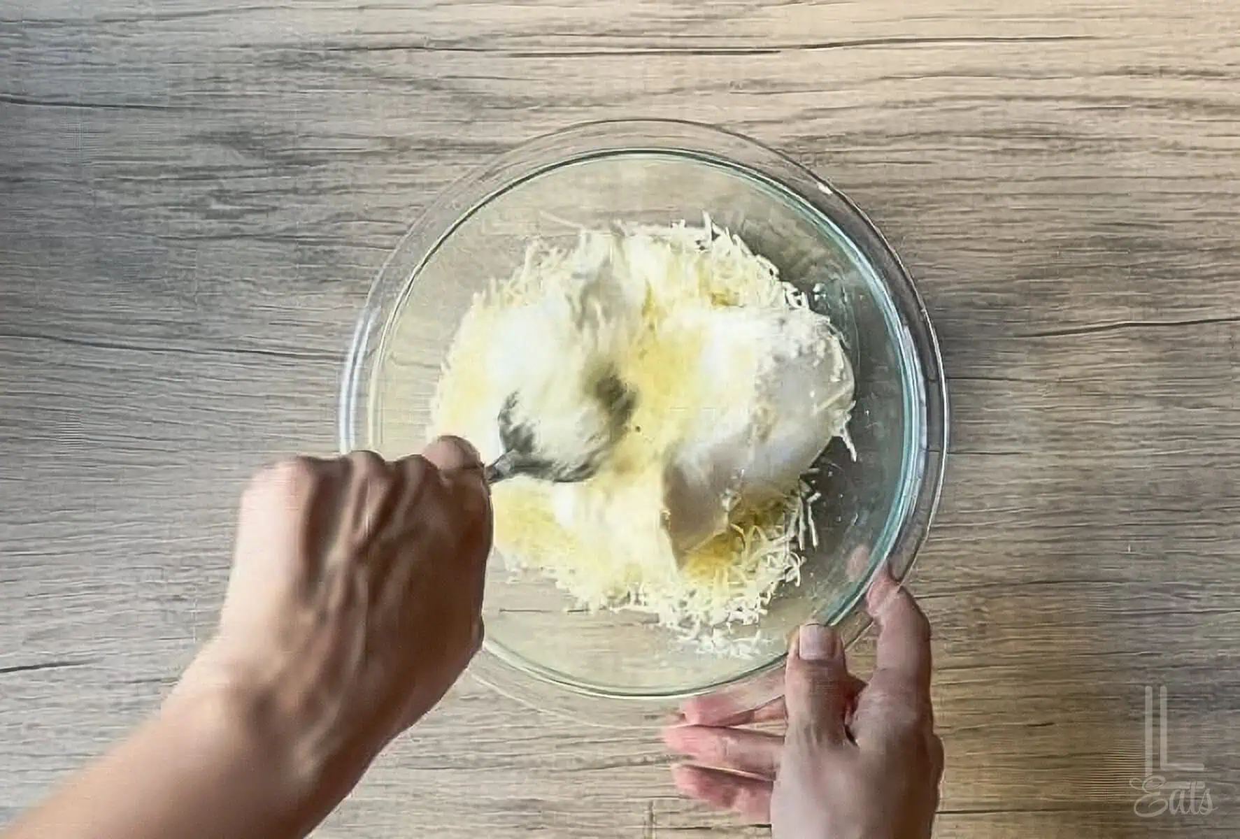 Mixing shredded parmesan and mozzarella cheeses with ricotta cheese in a glass bowl.