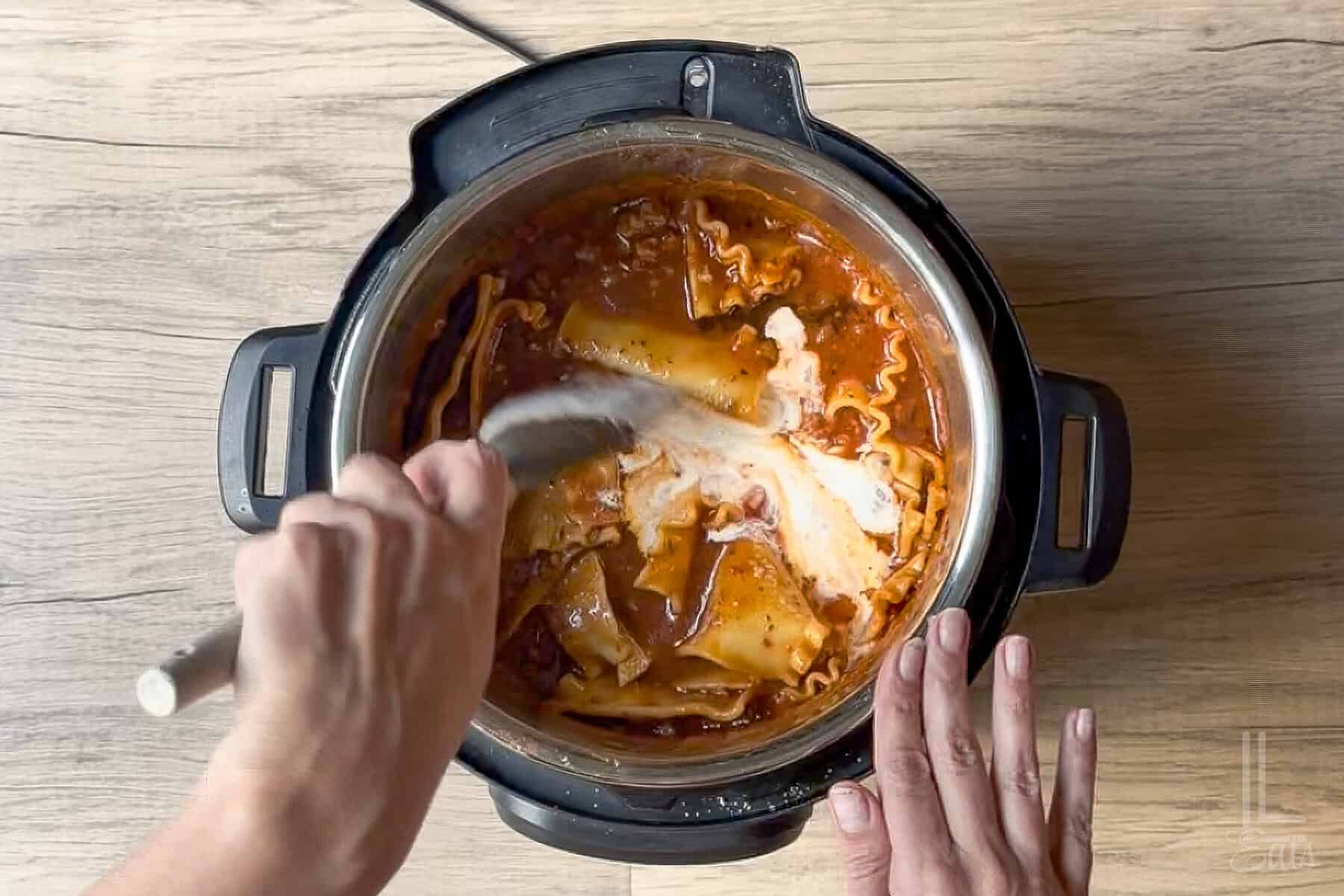 Adding heavy cream to the cooked lasagna soup in the instant pot.