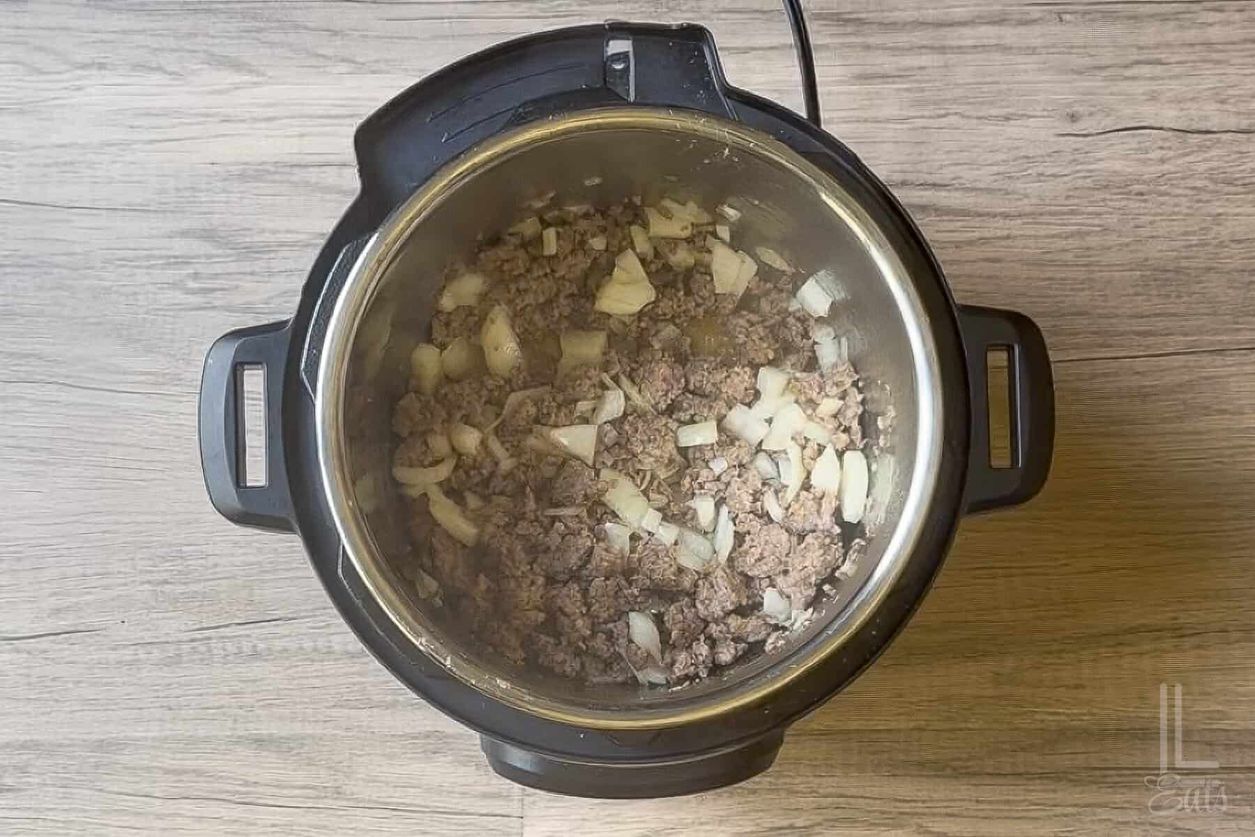 Italian sausage, onions, and garlic cooking in an Instant Pot for lasagna soup.