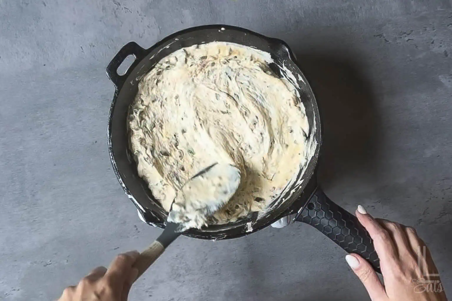 Smoothing creamy jalapeño popper dip into an even layer in a cast-iron skillet.