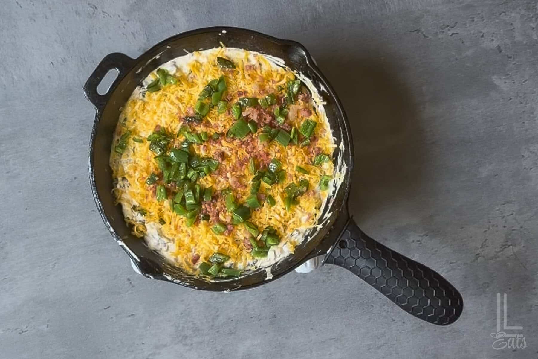 Jalapeño popper dip in a skillet topped with cheese and sauteed jalapenos.