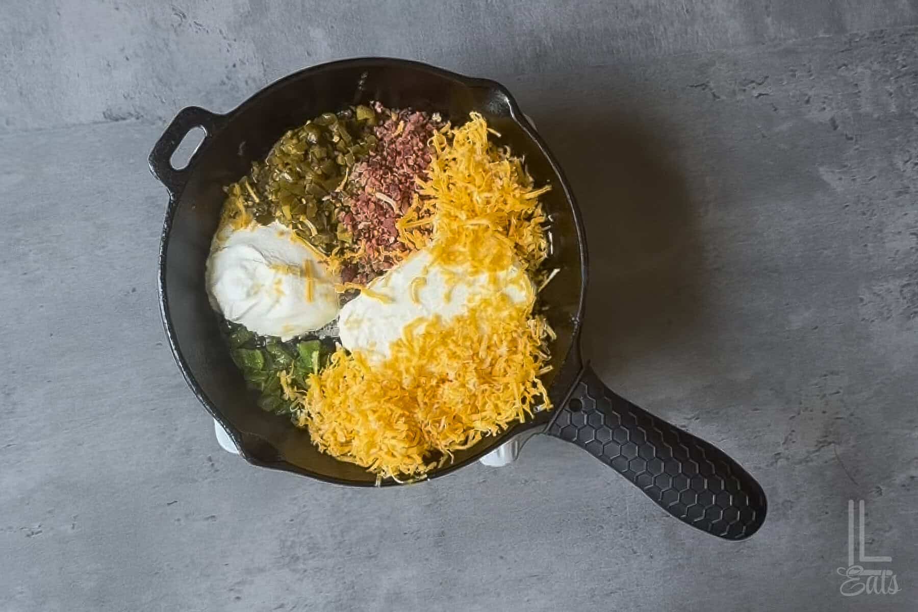 Jalapeño Popper Dip ingredients in a skillet with shredded cheese , cream cheese, and bacon.