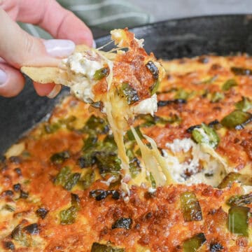 lifting a scoop of jalapeno popper dip with a tortilla chip.