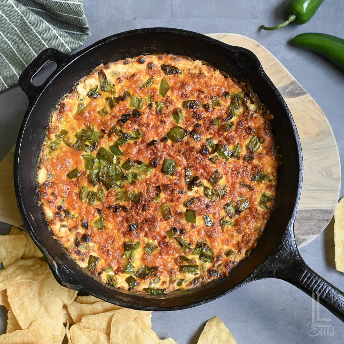 Jalapeño popper dip in a cast iron skillet with chips and jalapeños around it.