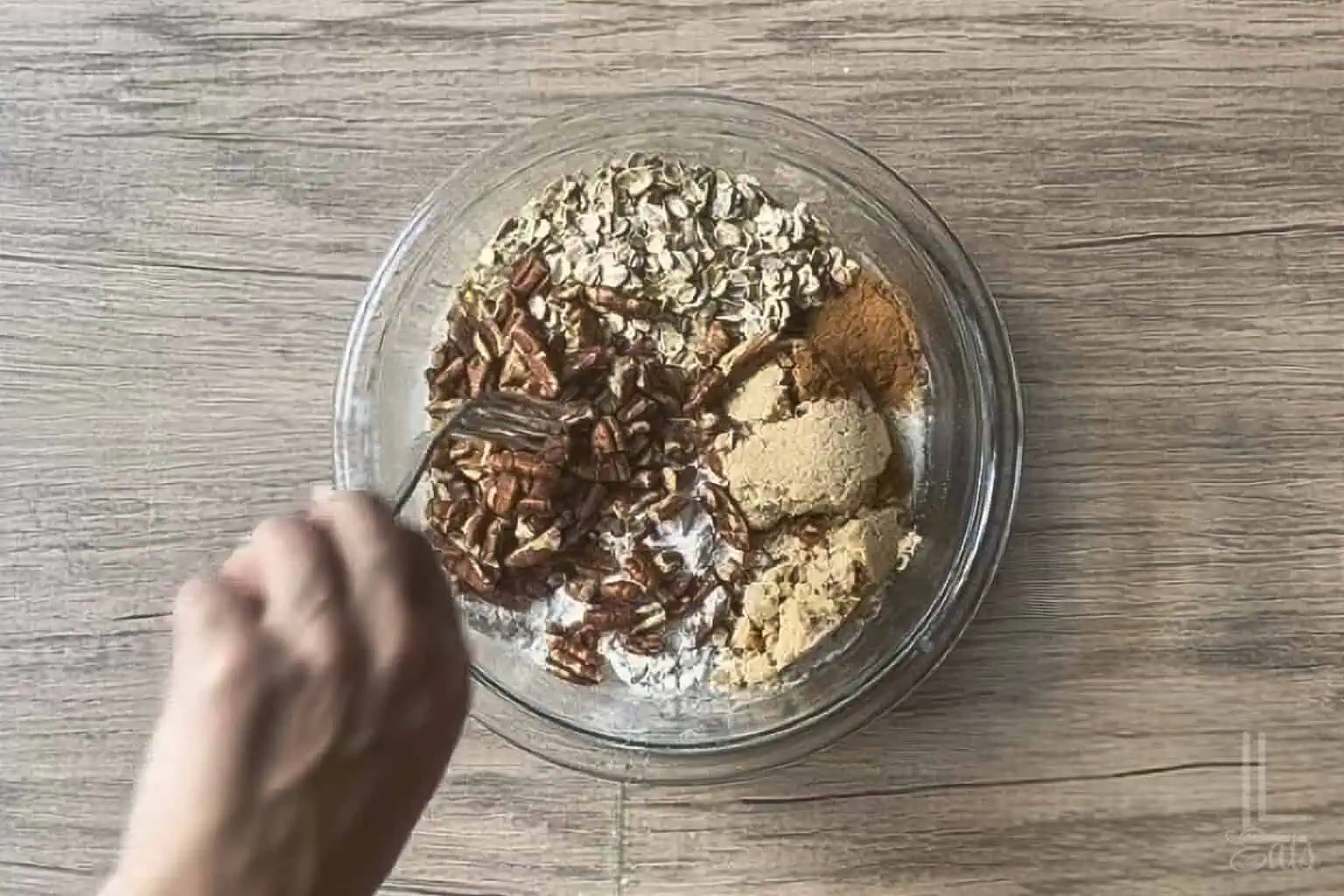 mixing flour, oats, pecans, butter, brown sugar, and cinnamon in a glass bowl.