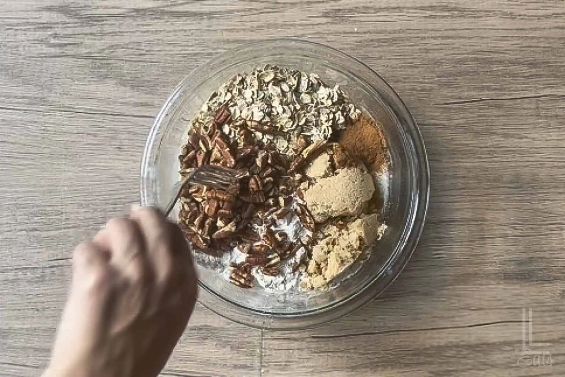 mixing flour, oats, pecans, butter, brown sugar, and cinnamon in a glass bowl.