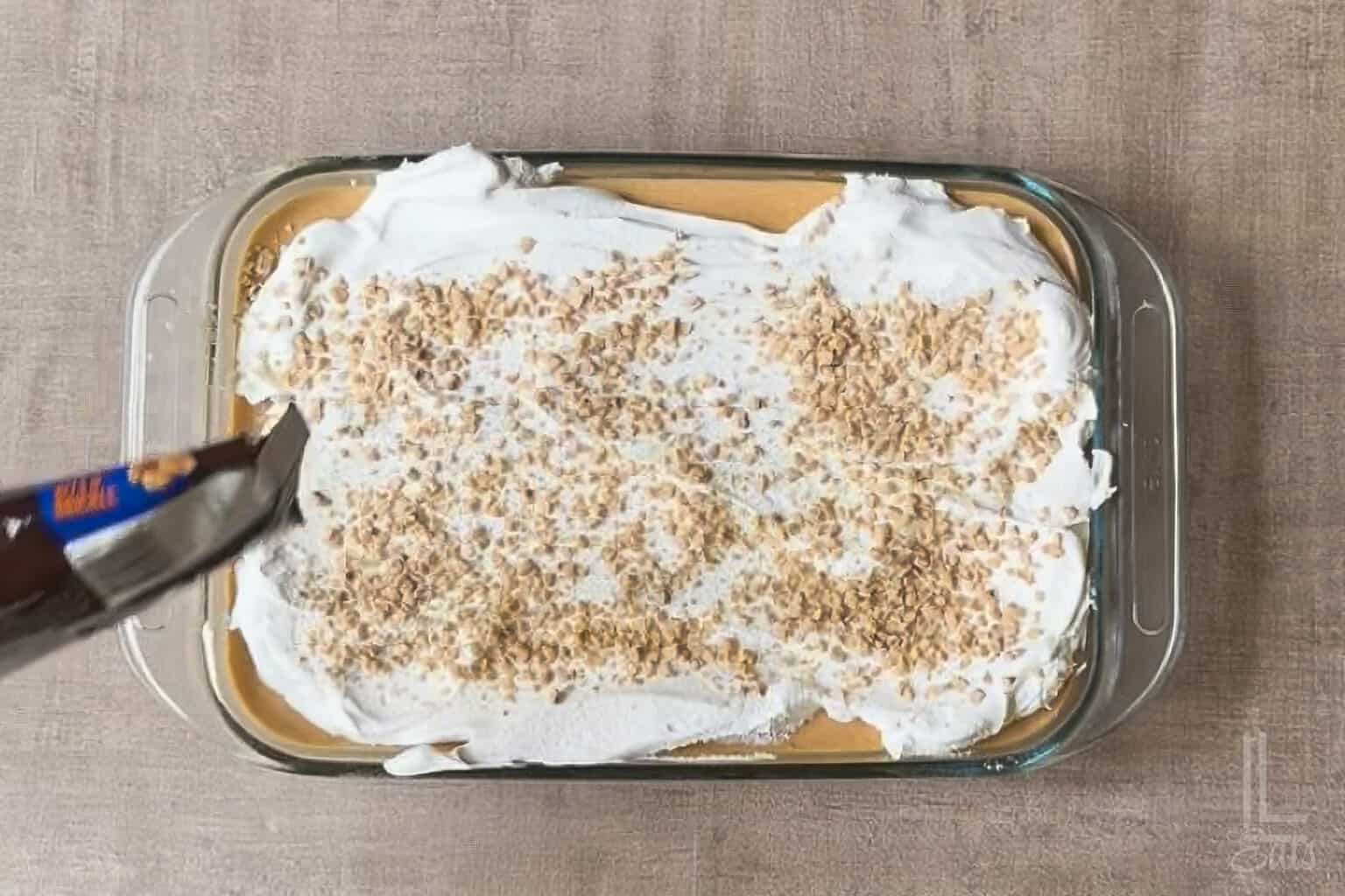 Pumpkin poke cake with whipped topping and toffee bits in a glass dish.