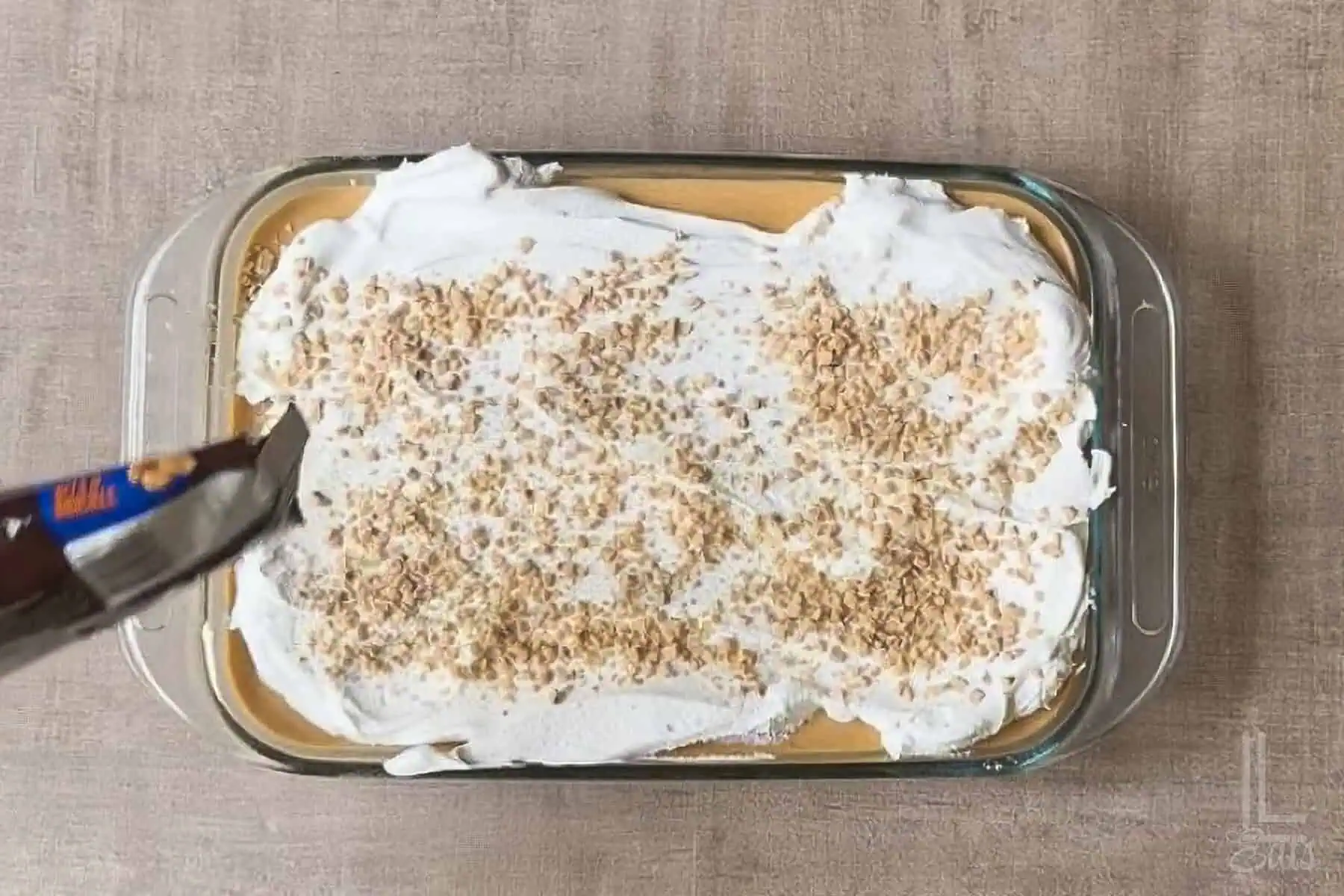Pumpkin poke cake with whipped topping and toffee bits in a glass dish.