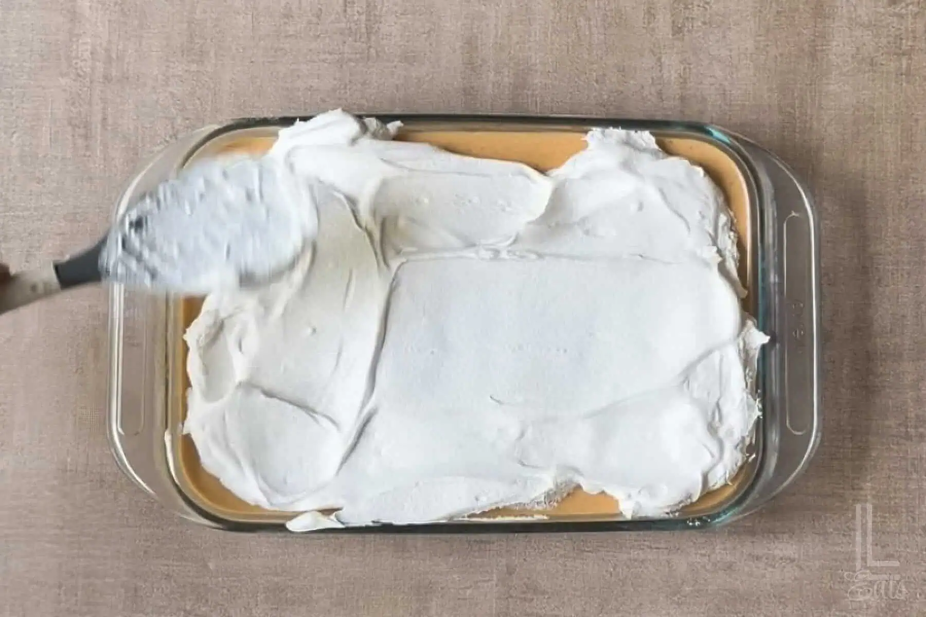 Whipped topping spread over pumpkin poke cake in a glass dish.