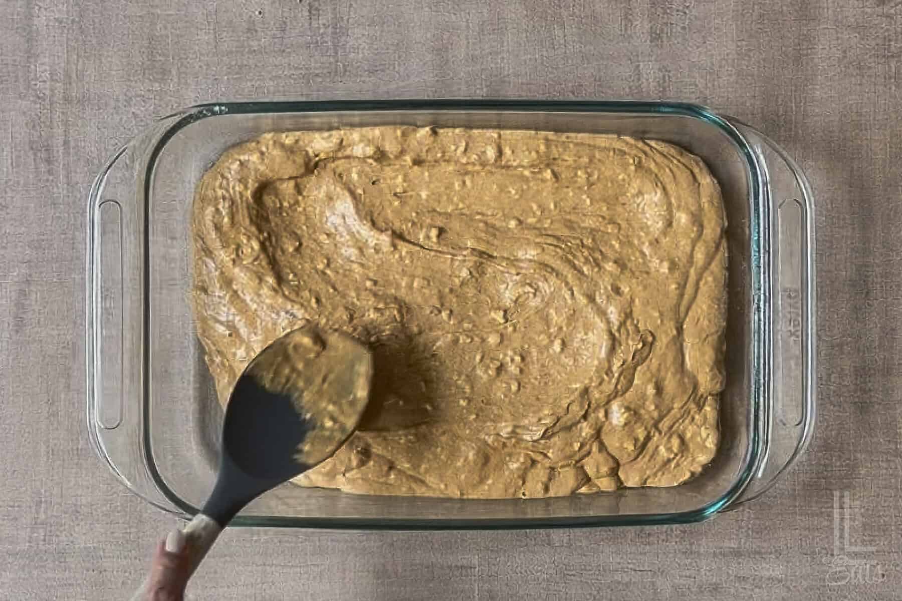 Pumpkin poke cake batter in a glass dish with a spoon for baking.