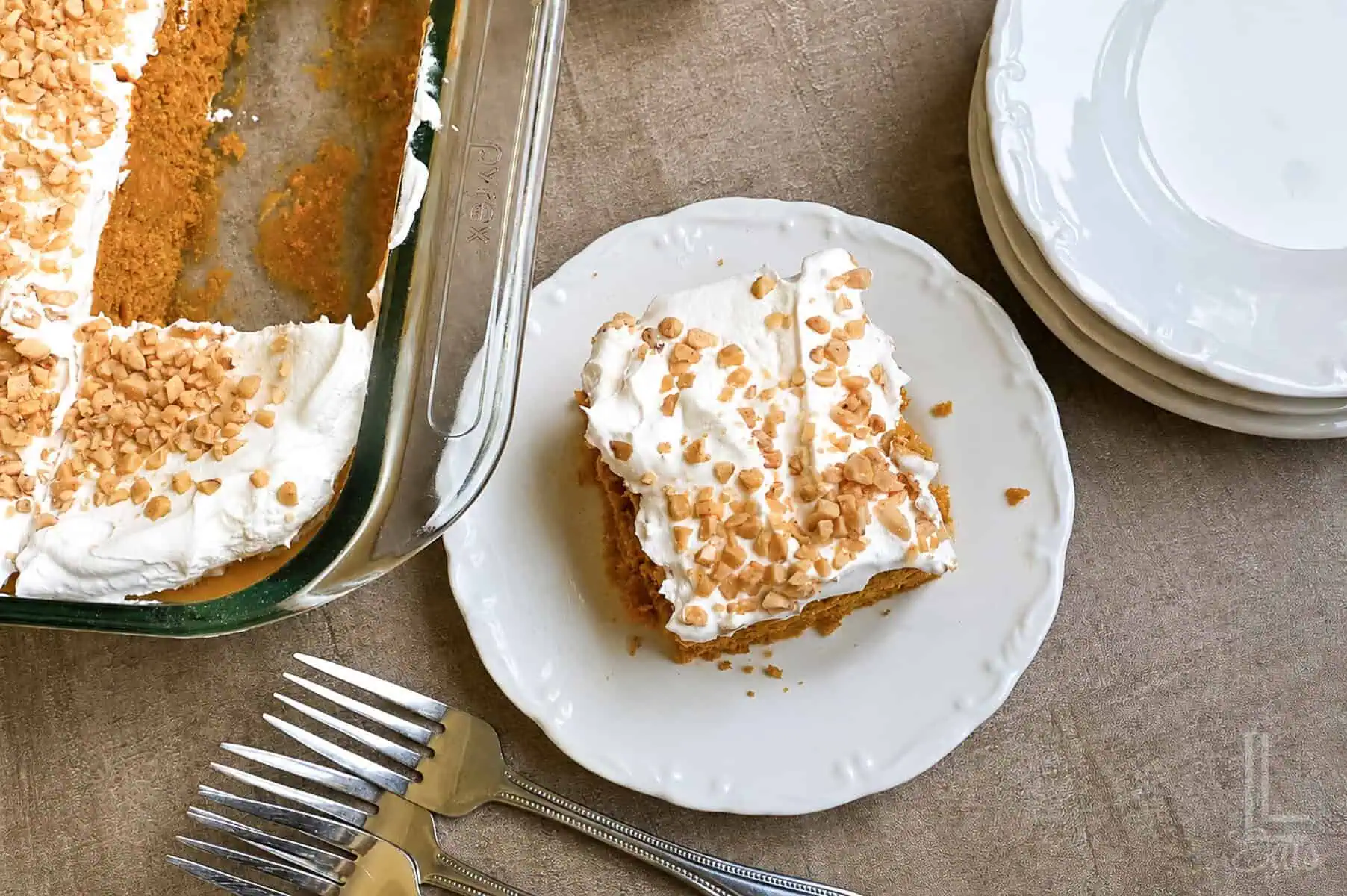 Slice of pumpkin poke cake with whipped topping and toffee bits on a white plate.