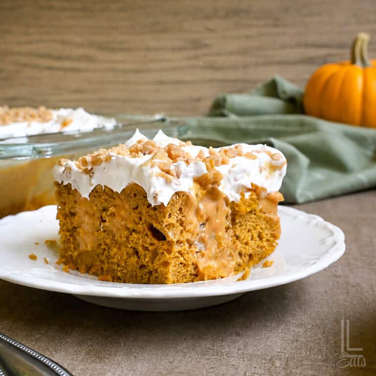 slice of pumpkin poke cake on a plate in front of a baking dish.