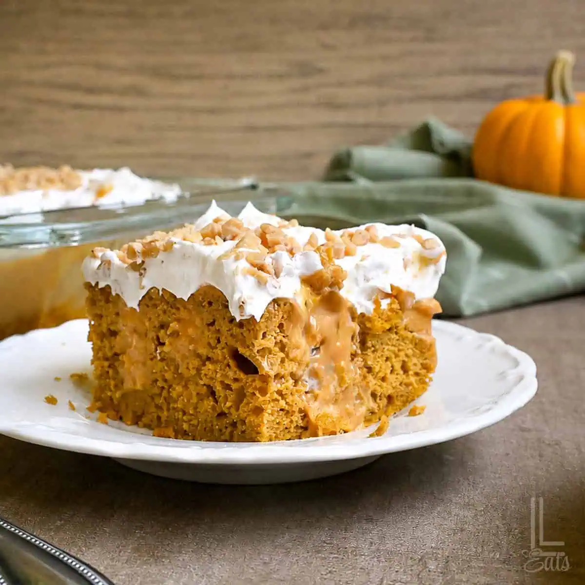 slice of pumpkin poke cake on a plate in front of a baking dish.