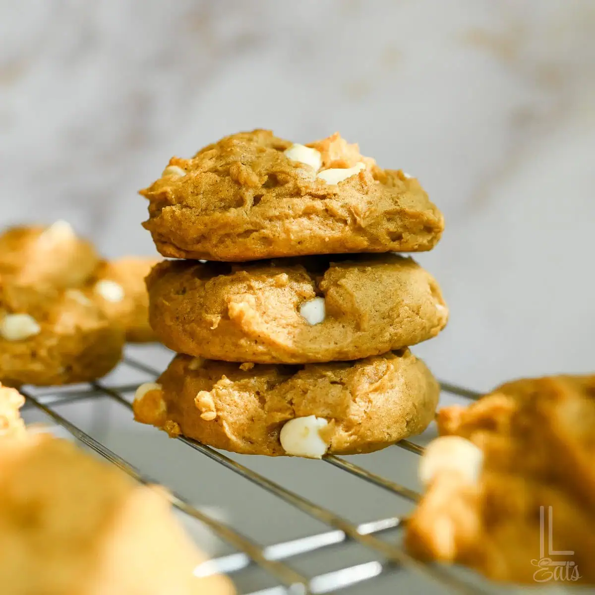 a stack of pumpkin white chocolate chip cookies on a baking rack.