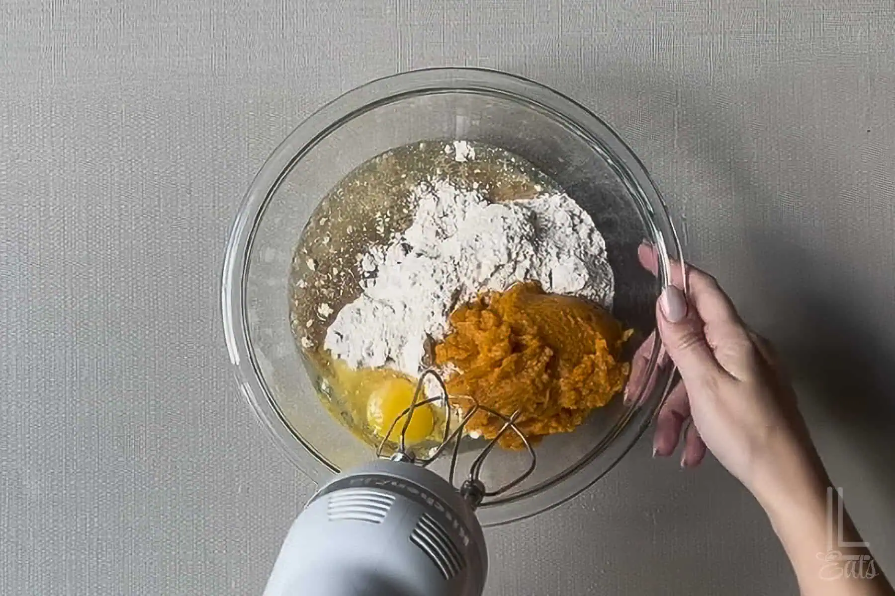 Mixing pumpkin, spice cake mix, and egg for pumpkin cookies in a glass bowl.