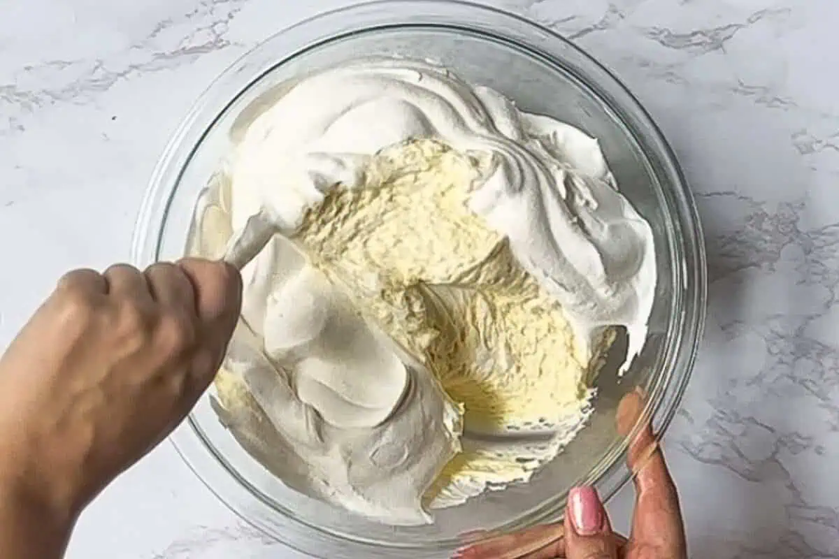 folding together whipped topping and cheesecake filling in a glass bowl.