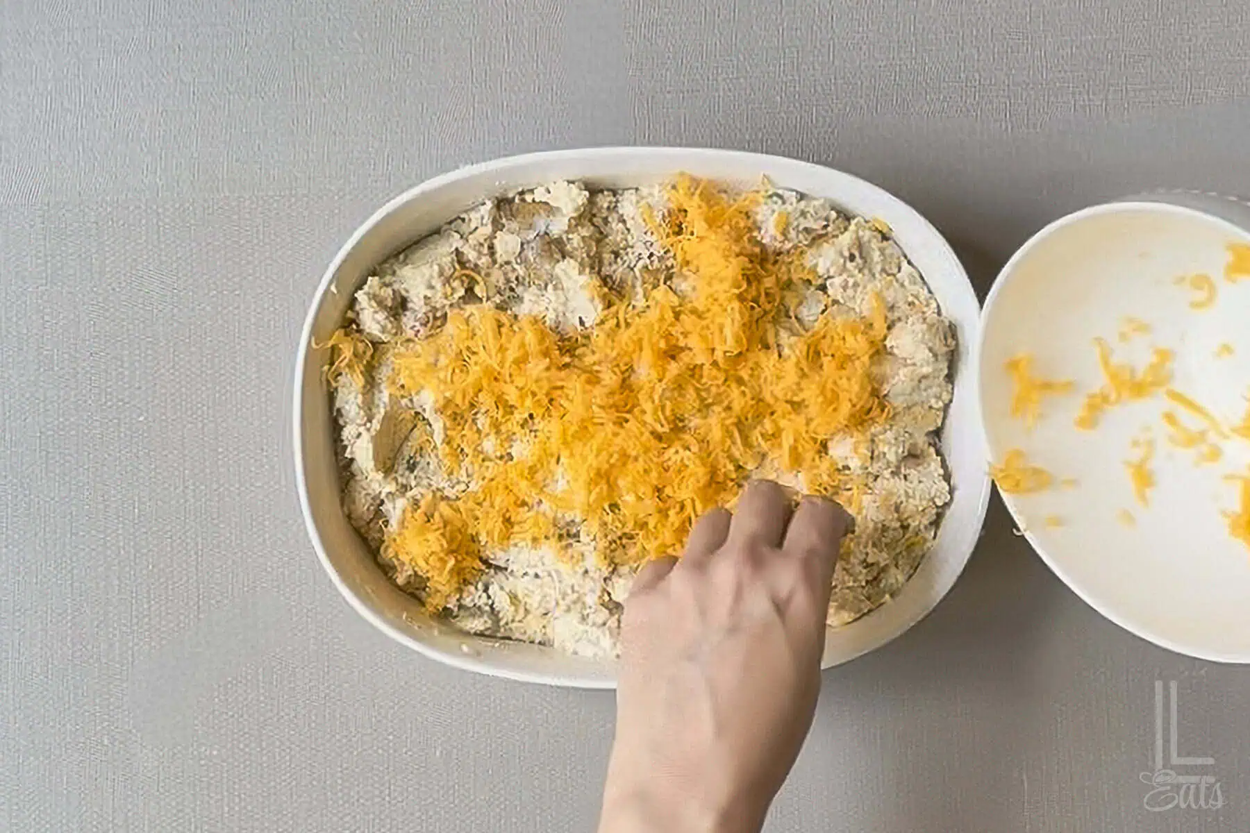 Spreading shredded cheddar cheese over the twice baked mashed potato casserole.