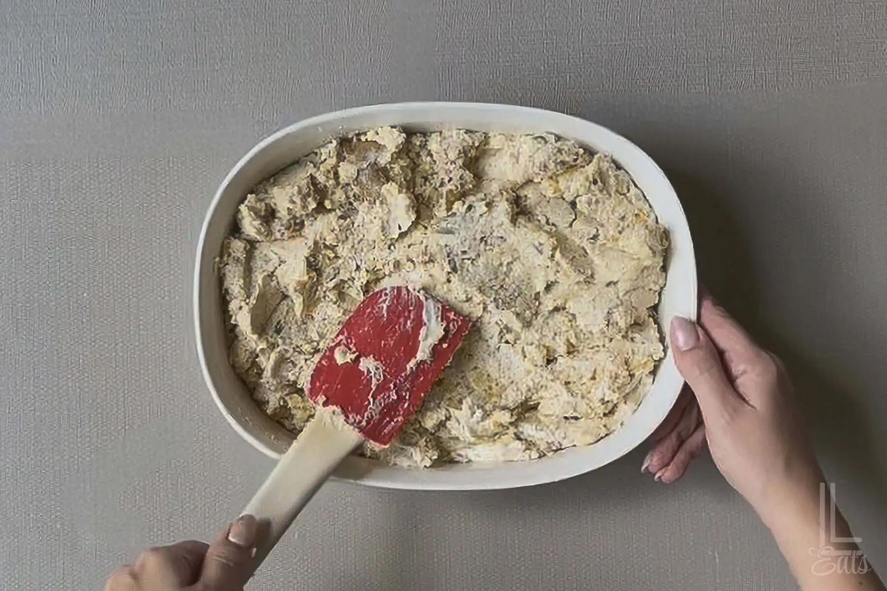 Spreading the twice baked mashed potatoes in a white baking dish with a spatula.