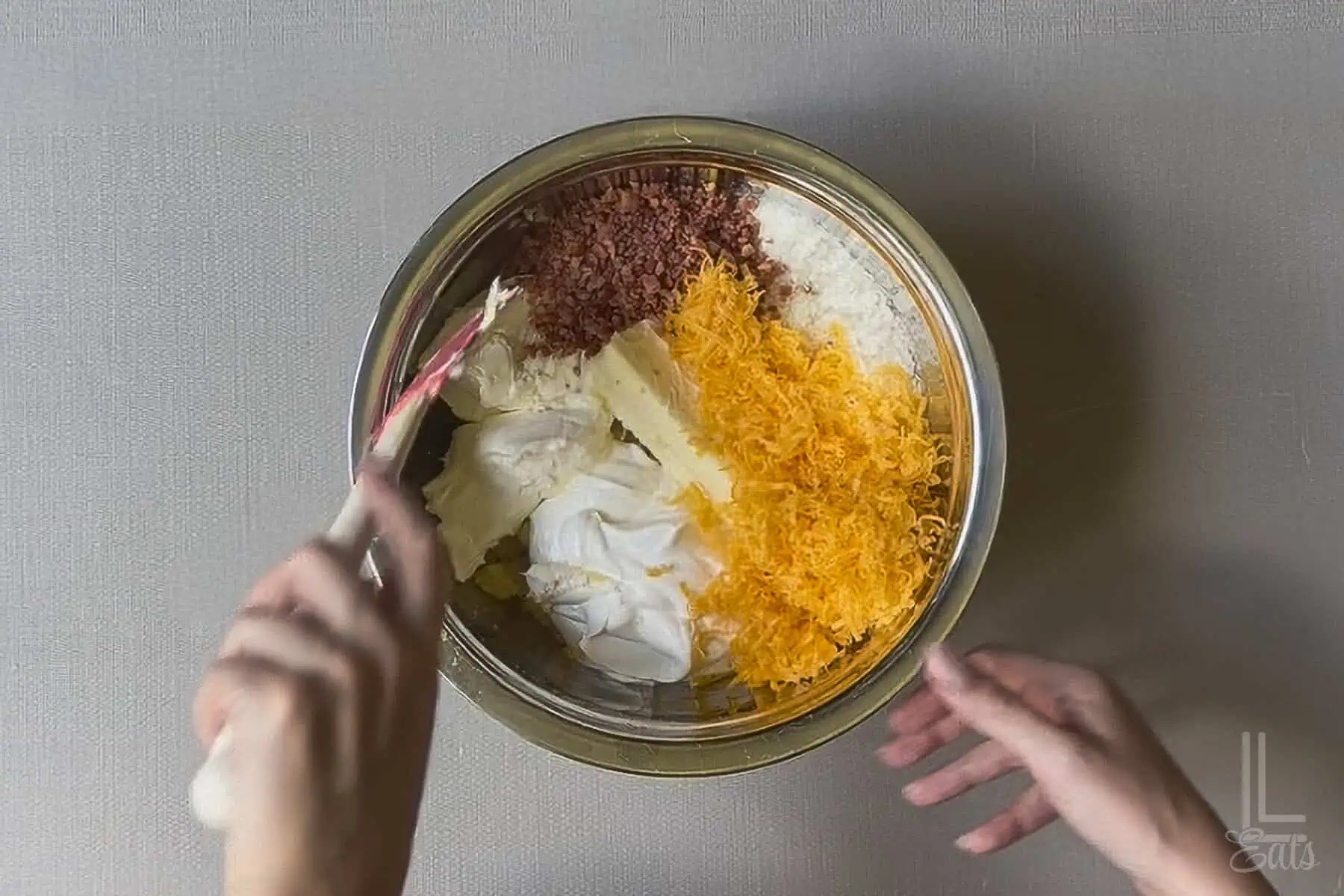 Bacon, cheese, potato flakes, and other ingredients added to mashed potatoes in a mixing bowl.