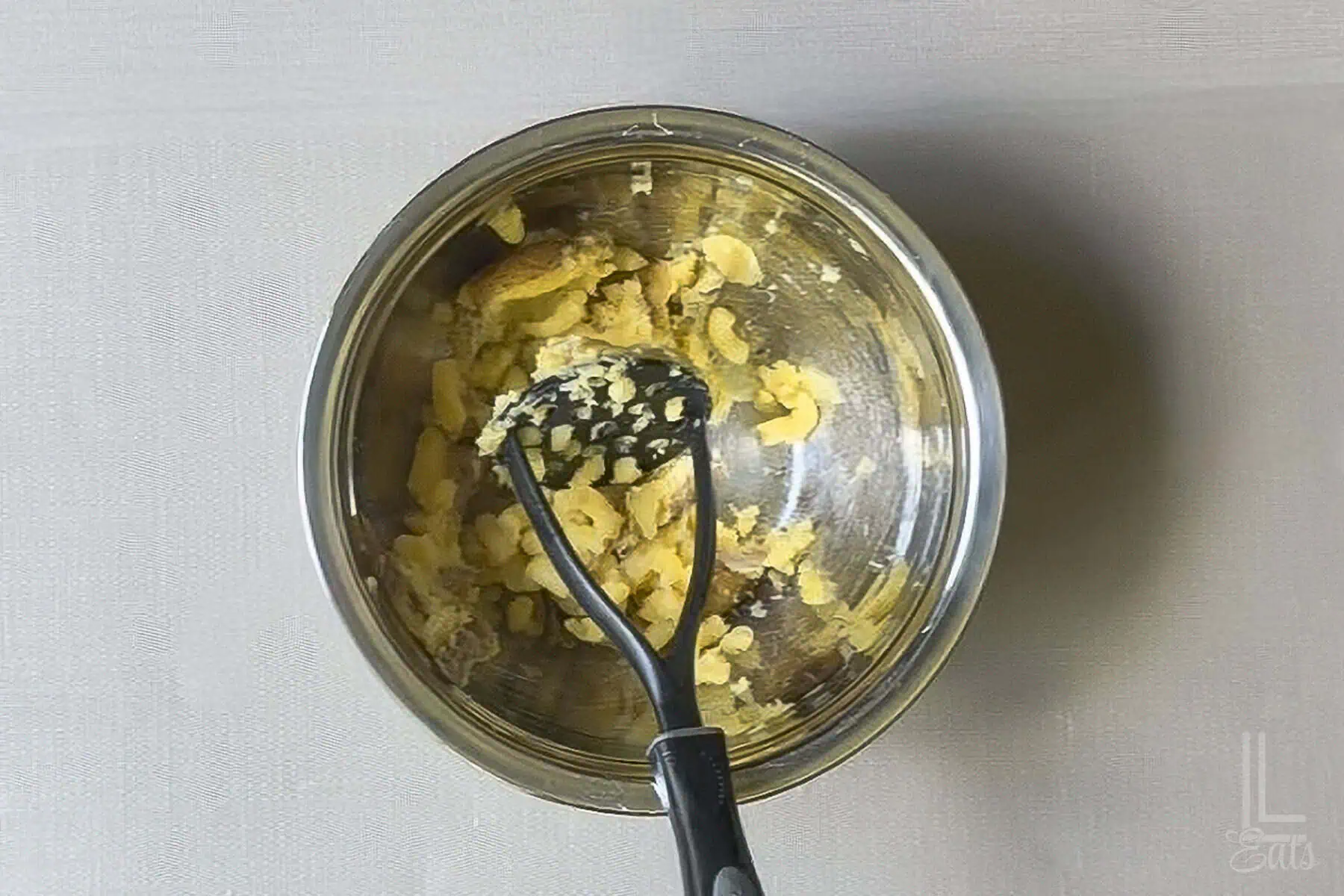 Mashed potatoes in a bowl with a potato masher on a gray surface.