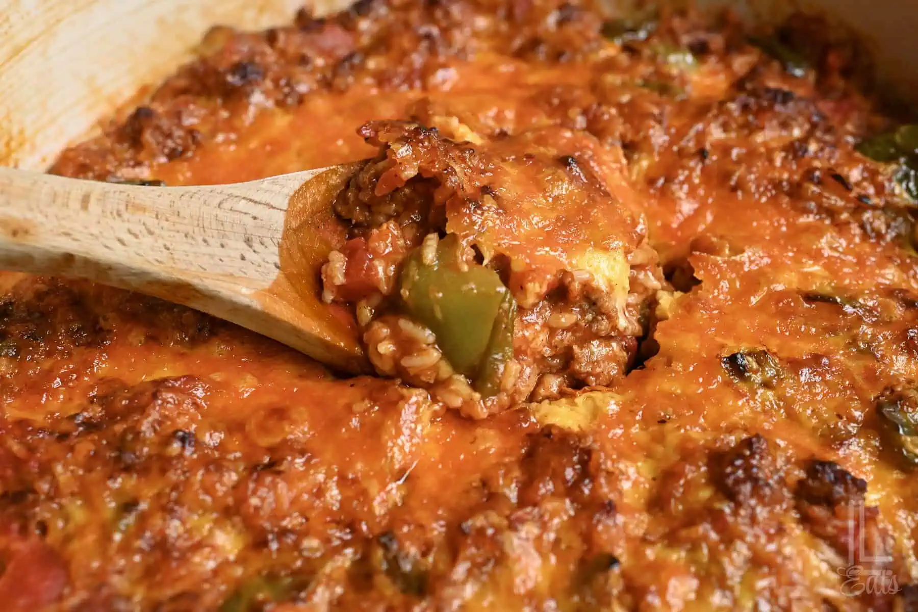 a wooden spoon in a lot of unstuffed peppers topped with cheddar cheese.