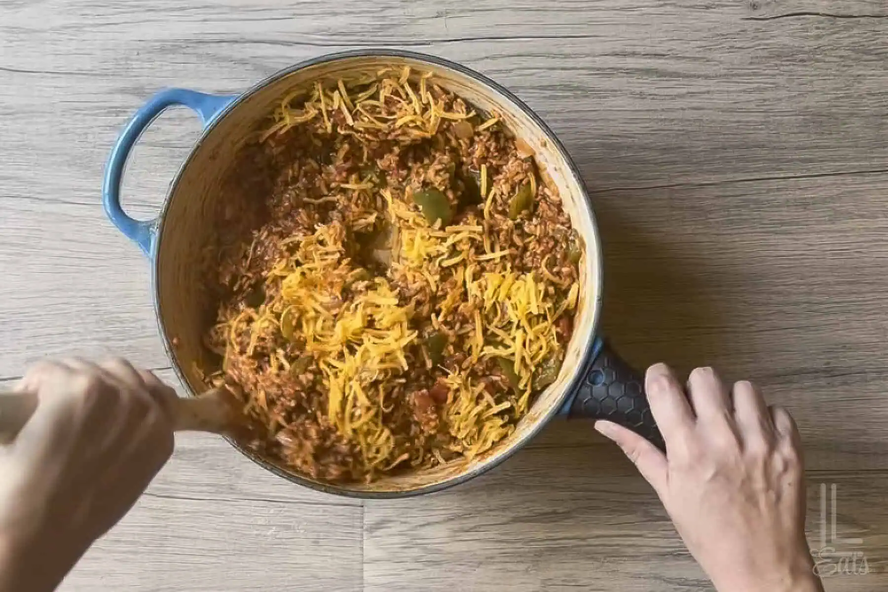 Stirring shredded cheddar cheese into the unstuffed pepper rice mixture.