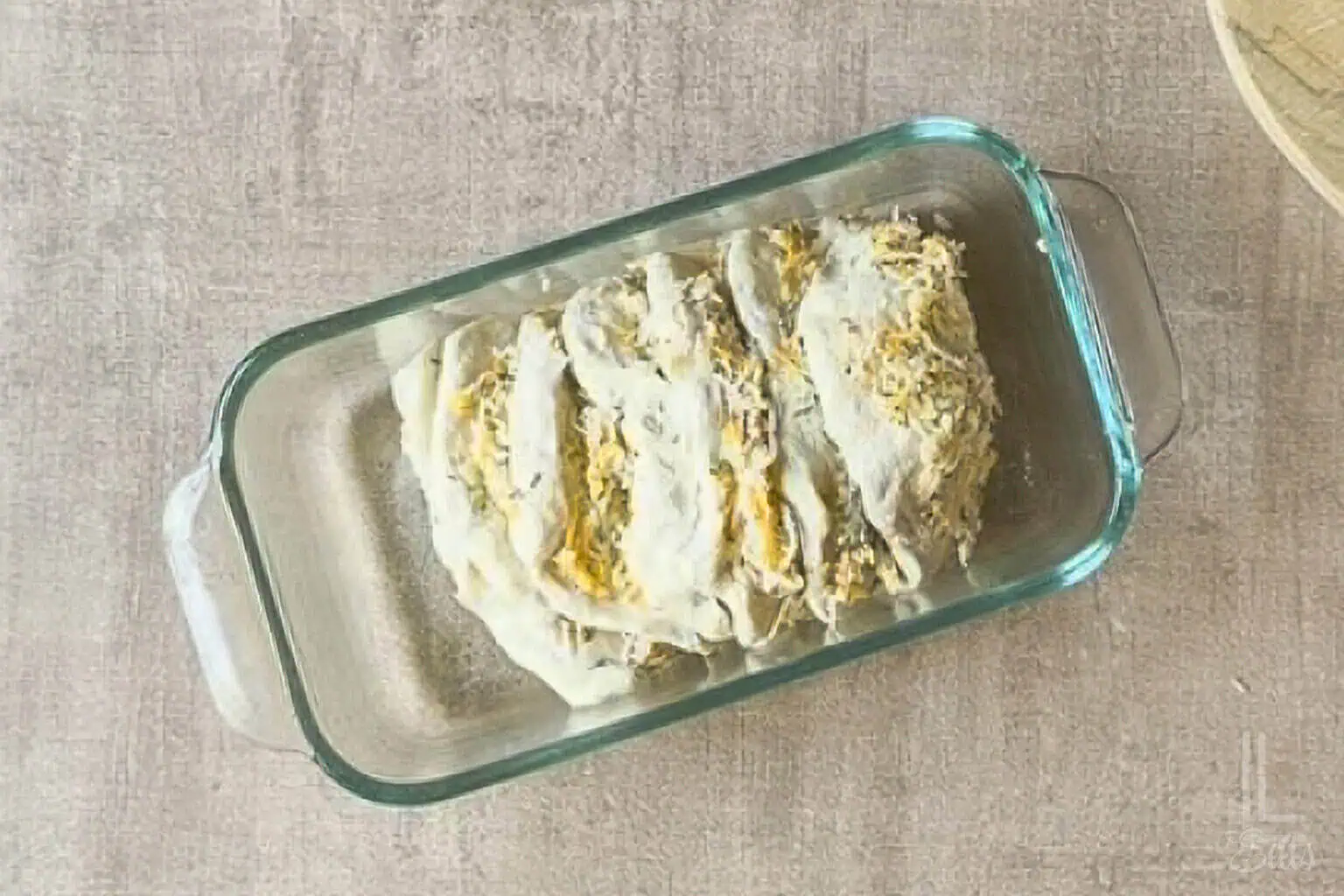 Unbaked cheesy garlic pull apart bread in a glass baking dish.